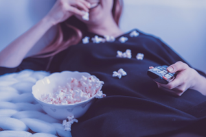 woman laying down holding remote and eating popcorn