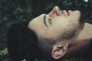Close up of a man laying down on the forest floor looking at the sky.