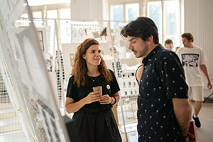 a man and a woman standing in front of a painting. the man is looking at the painting and talking with the woman. 