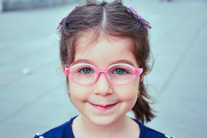 a little girl is smiling and wearing pink glasses with oval frames. 